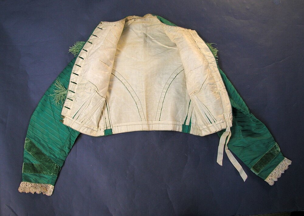 Inside of a green silk 1860s jacket showing its cream lining, front buttonholes and curved back seams