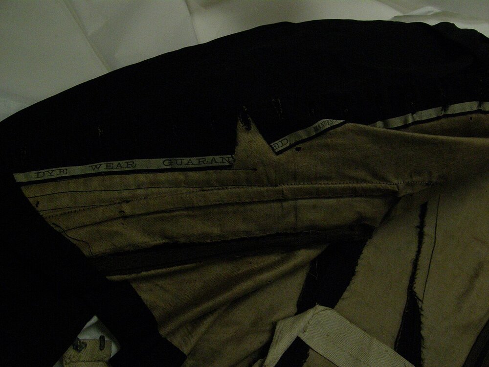 Inside of a black silk satin bodice showing a tan lining, a printed selvedge and cut seam edges