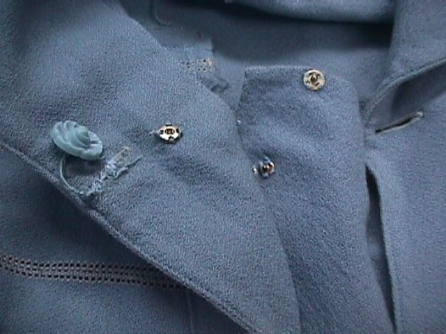Front opening of a blue wool crepe dress showing a moulded blue button and two metal snap fasteners